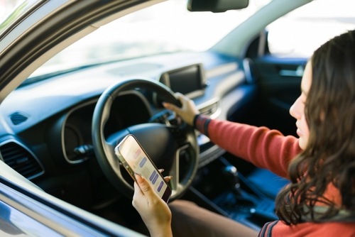 Teenage driver holding smartphone beside steering wheel inside car interior