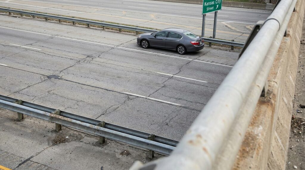 sedan driving on cracked multi-lane highway near Kansas City Street sign