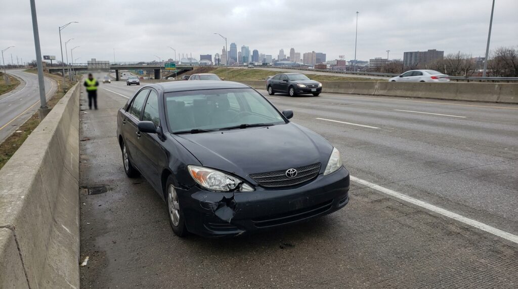 Toyota sedan with front-end collision damage stopped on urban highway shoulder